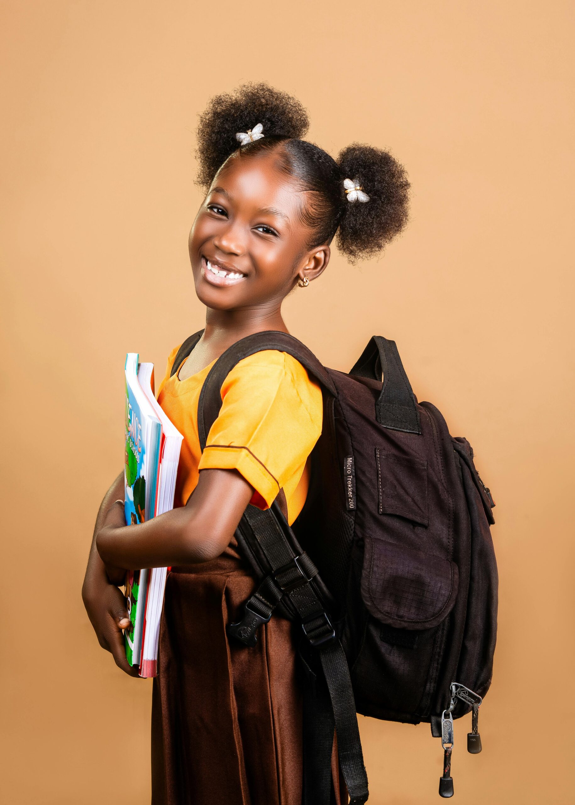 Cheerful African girl with backpack embracing books, ready for school.